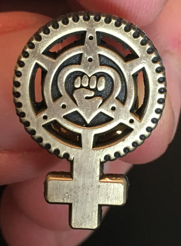 a pin in the shape of a woman symbol, with the circle as a bike chainring and a fist in the center