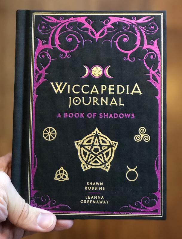 Cover of Wiccapedia Journal: A book of Shadows, which is black with purple and gold accents - primarily various pagan symbols