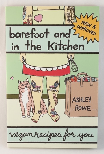 A book with an illustration of a barefoot person with tattoos in an apron and a cat at their feet