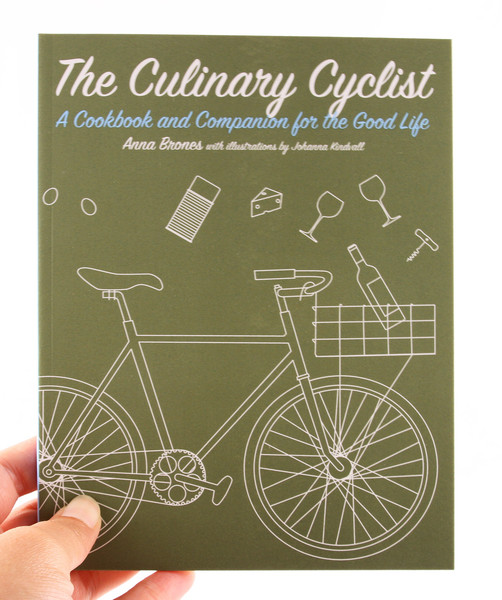 A green book with white, outlined illustration of a bicycle with a basket. A bottle of wine, glasses, corkscrew, and other necessities are either flying out of the basket or into it