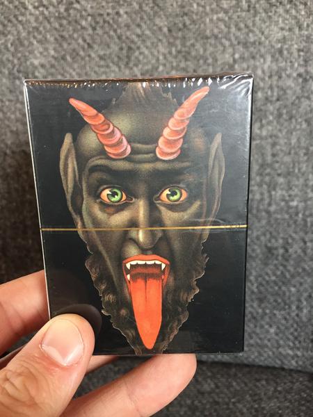 Krampus Playing Cards: 52 Vintage Designs by Monte Beauchamp (An illustration of a dark and evil looking Krampus with horns, bulging eyes, a long, red tongue, and fangs)