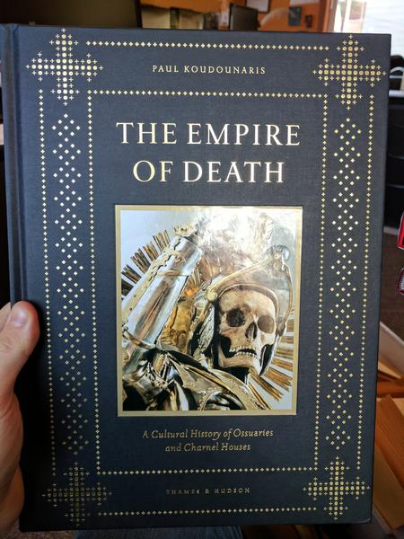 The Empire of Death: A Cultural History of Ossuaries and Charnel Houses by Paul Koudounaris (a black cover with gold lettering and detailed border. In the middle is a photograph of a skeleton in silver and gold armor)