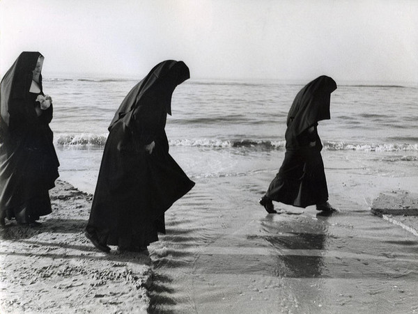 a vintage photo of three nuns wading into a body of water