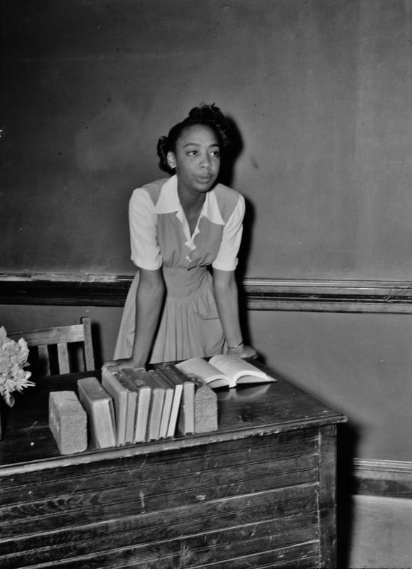 a teacher stands at a desk, reading from a book