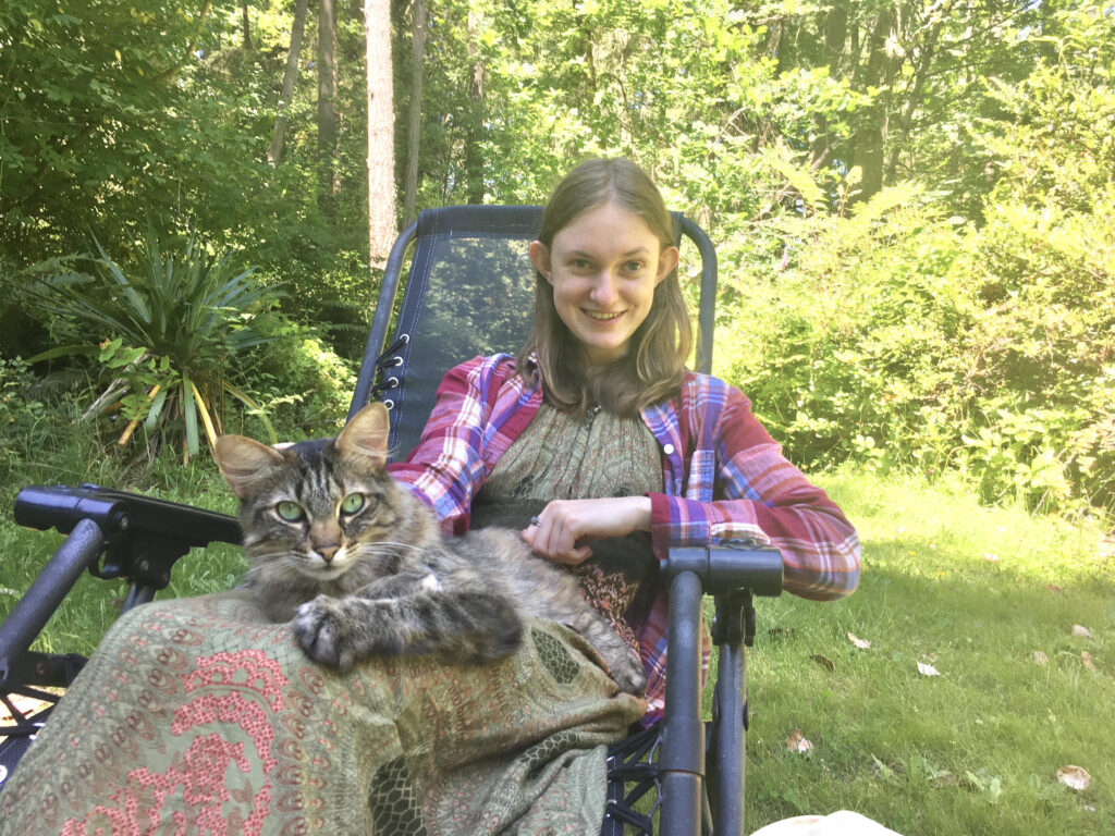 a young woman sits in a lawn chair with a cat on her lap