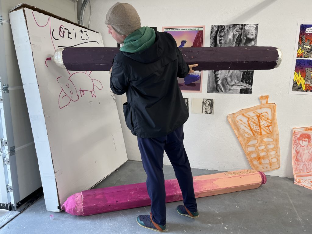 A tall publishing professional draws with a gigantic pen at a gallery space