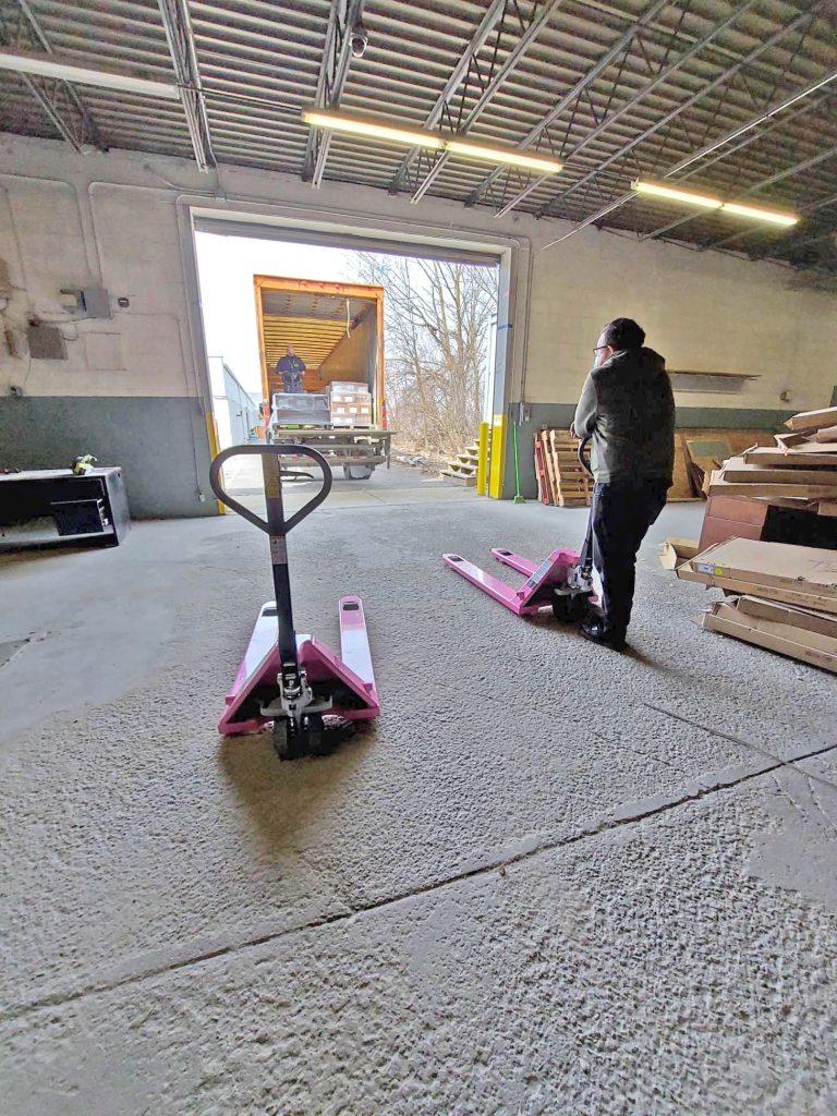 a worker pensively waits with two pink pallet jacks for a truck to unload pallets