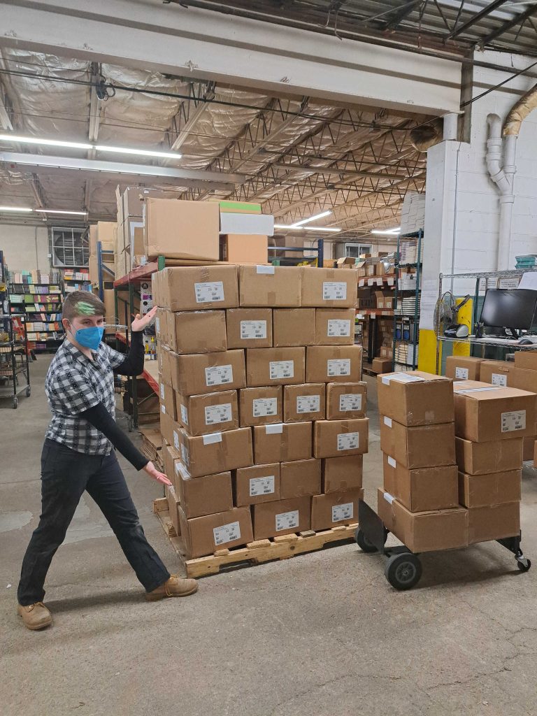 a microcosm warehouse worker with green hair shows off a large pallet of outgoing mail
