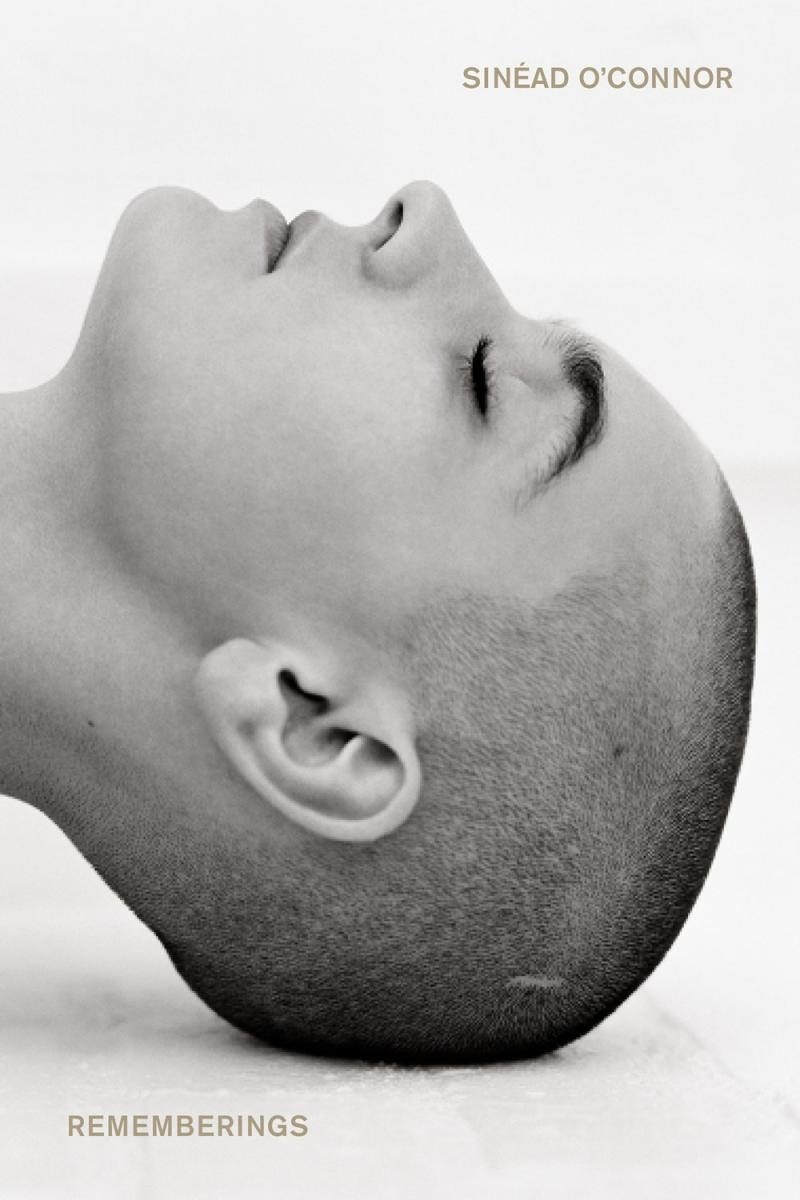 A black and white photo of a young Sinead O'Connor's head laying down from the side. 
