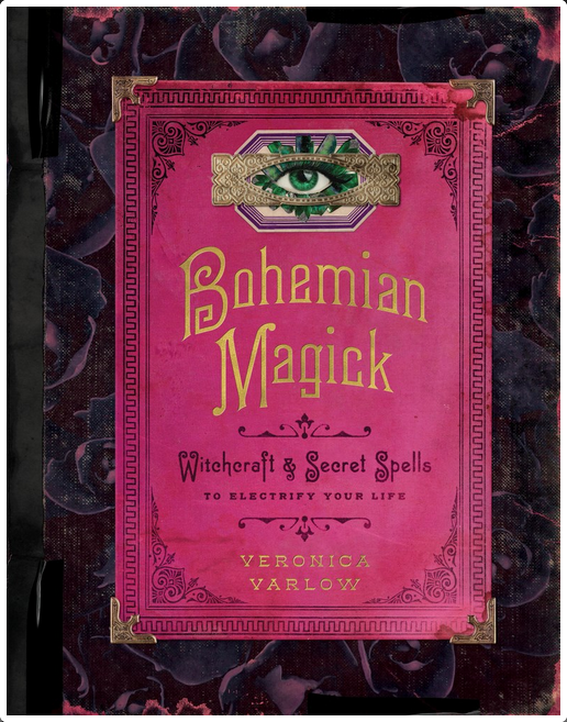 Pink cover with black and gold text with an image of an eye framed by crystals above the title. There is a border of dark purple petals.