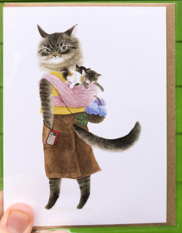 A grey cat wearing a papoose on her back filled with kittens.