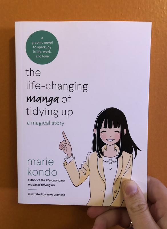 A manga-version of author Marie Kondo, smiling and pointing her finger to the title. 