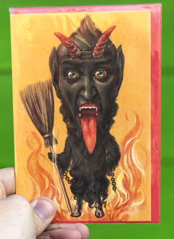 A devilish goat-like figure stands engulfed in flames, clutching a broom in his hand.