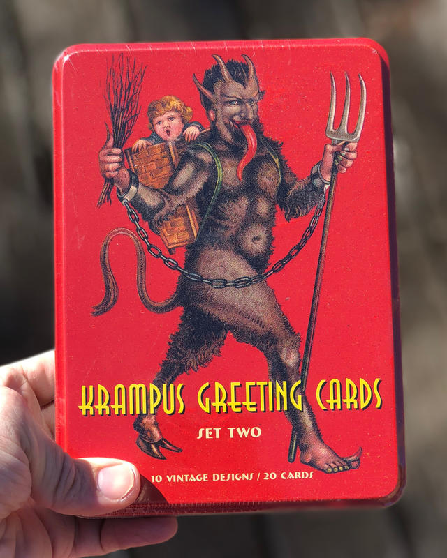 Krampus holding a pitchfork, with a kid in his back in a basket.