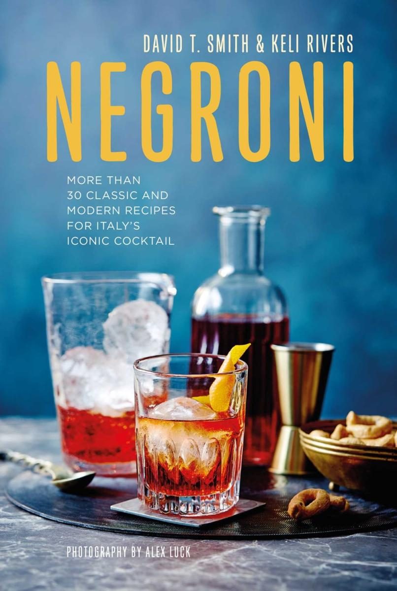 negroni in the center, flanked by two other glasses, a mixing cup and some bar snack thingies