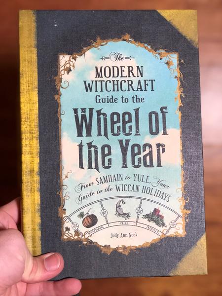 Modern Witchcraft Guide to the Wheel of the Year, The: From Samhain to Yule, Your Guide to the Wiccan Holidays by Judy Ann Nock [A cloudy sky drifts above a wheel of rotating pagan holidays]