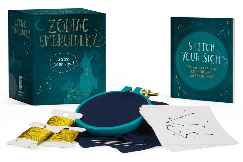 an embroidery hoop, needles, gold floss, pattern sheets, and dark blue box for the kit with constellations on it.