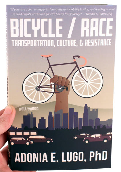bicycle race book cover featuring a fist holding a bicycle above the LA skyline