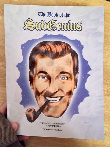 Cover of The Book of the SubGenius: The Sacred Teachings of J.R. 'Bob' Dobbs which features a drawing of a masculine head smoking a pipe and smiling