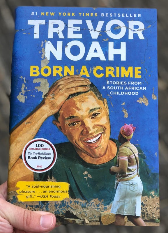 A black woman looking at an illustration of Trevor Noah on a brick wall.