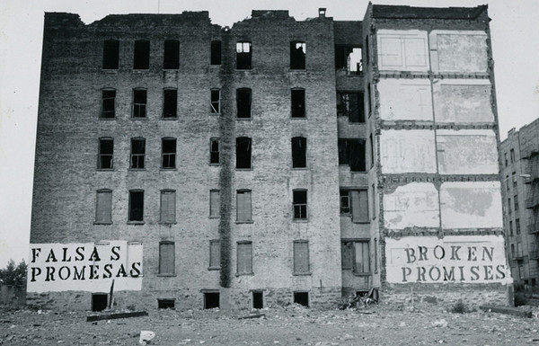 blighted building with murals reading "falsas promesas" and "broken promises"
