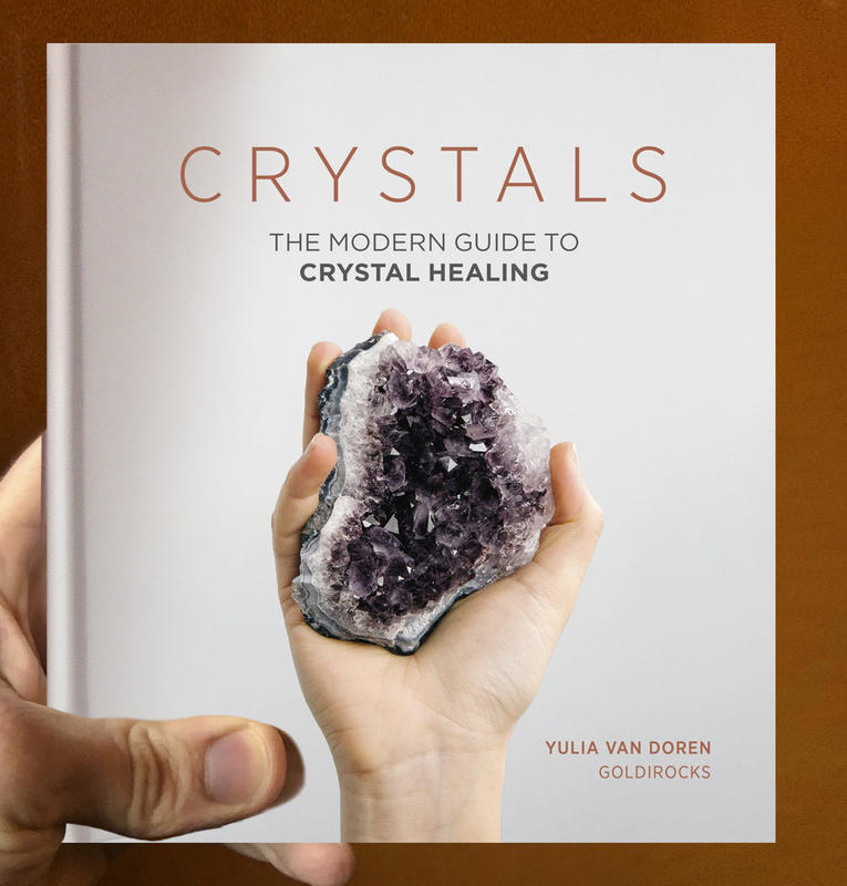 grey book with a hand holding a purple crystal and shiny font
