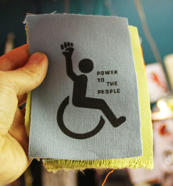 canvas patch with a person in a wheelchair raising their fist and the text "power to the people"
