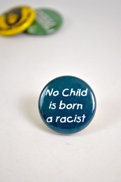 Button / pin that reads No Child is born a racist
