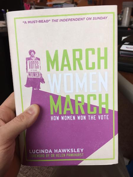 A white and purple book cover with a woman holding a sign that says, "Votes For Women."