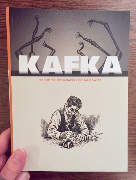 A book cover depicting Franz Kafka writing with a pen on a table writing on the bottom half of the cover, while the top cover shows the body and legs of a bug laying on it's back