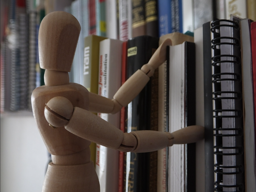 a wooden drawing figure seems to be pushing a book into the shelf
