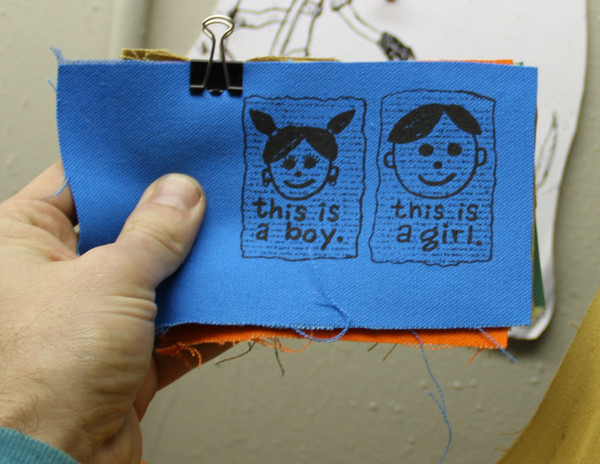 patch with a person with pigtails and earrings sayingthis is a boy and one with a short haircut saying this is a girl 