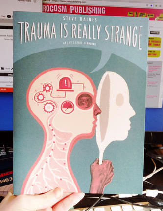 Cover of Trauma is Really Strange which features a human bust in profile holding up a mask over its face. Inside the head, there are gears and alarms. 