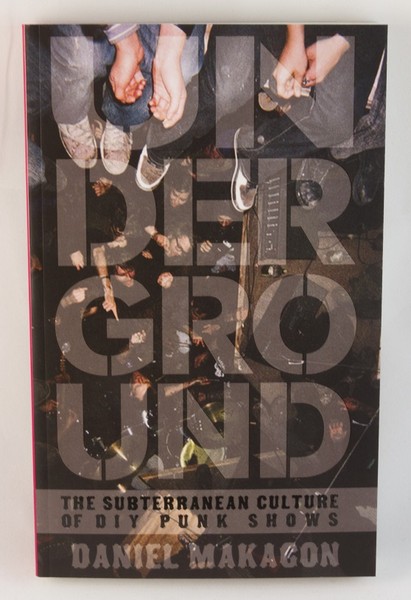 A black book cover with a photo of the legs of people sitting on a balcony over the heads of show-goers. The text is transparent